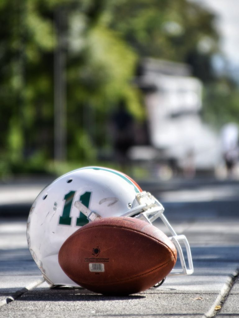 football helmet beside football on gray asphalt road